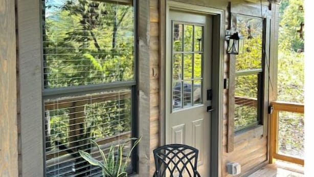 A wooden porch with a door, two chairs, a small table, and a potted plant. - Bear Top Junior Small Cabin w EV Charger

 (Cosby)