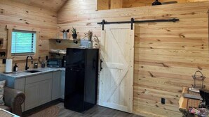 A compact kitchen with wooden walls, a black refrigerator, and a sliding barn-style door. - Bear Top Junior Small Cabin w EV Charger

 (Cosby)