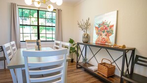 A dining area with a table, chairs, a vase, a painting, and a console table with a basket. - Hot Tub Retreat by Wine Country (Fredericksburg)