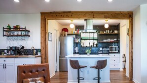 A modern kitchen with a central island, bar stools, a refrigerator, and a coffee machine. - Hot Tub Retreat by Wine Country (Fredericksburg)