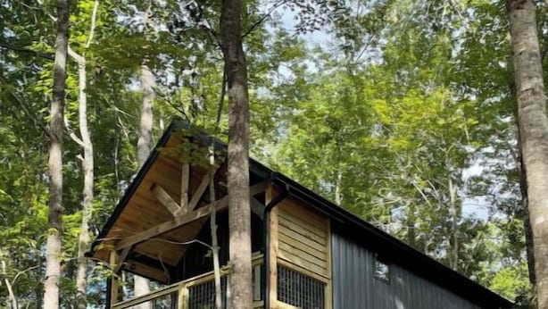 Une cabane en bois à deux étages, dotée d’un balcon et entourée d’arbres.