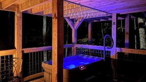 Une terrasse en bois avec un jacuzzi, une rambarde en métal et une chaise.