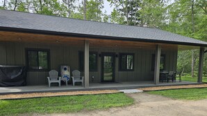A covered outdoor seating area with Adirondack chairs and a table, surrounded by a wooden deck and a grassy lawn. - NEW 3-bedroom cabin in beautiful Emily, MN.  Located right on the trails! (Emily)