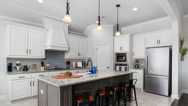 A modern kitchen with white cabinets, a large island with bar stools, stainless steel appliances, and pendant lighting. - The Noble House Near Magnolia with Pool (Hewitt)