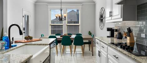A modern kitchen with white cabinetry, a granite countertop, and a dining area with green chairs.