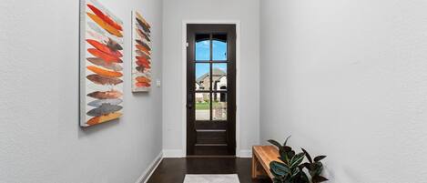 A hallway with a white wall, a dark wooden floor, a white rug, a bench, and a potted plant.