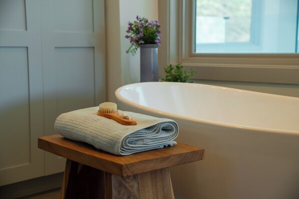 A bathroom with a bathtub, a wooden stool with a folded towel and a brush, and a potted plant.