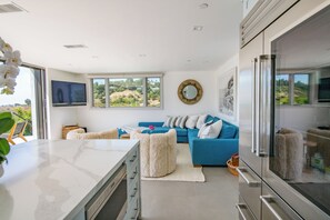 Una sala de estar moderna con un sofá azul, una mesa de centro blanca y un área de cocina con refrigerador y horno.