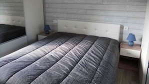 Ein Schlafzimmer mit einem Bett, einem Nachttisch, einer Lampe und einem an der Wand befestigten Spiegel.