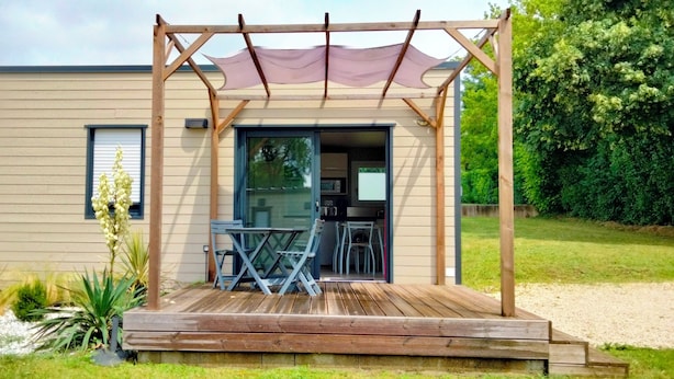 Ein modernes Haus mit einer Holzterrasse, einer Pergola und einer kleinen Außenküche.