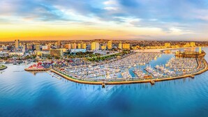 A marina with numerous boats docked, surrounded by a cityscape with modern buildings and a waterfront promenade.