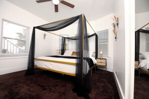 Ein Himmelbett mit dunklem Teppich, Deckenventilator und Nachttisch mit Lampe.