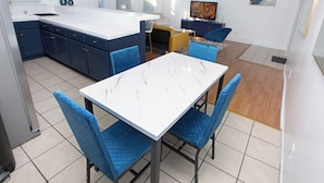 A modern kitchen with a white marble countertop, blue cabinetry, and a dining area with blue upholstered chairs.
