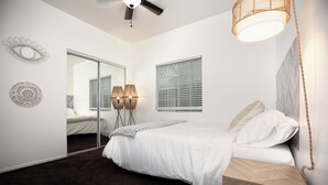 A bedroom with a bed, a mirror, a ceiling fan, and a window with blinds.