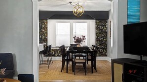 A dining area with a wooden table and chairs, a vase with flowers, and a ceiling light fixture.