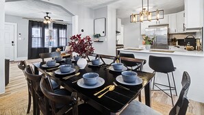 A modern kitchen with white cabinets, a stainless steel refrigerator, and a dining area with a black table set for six.