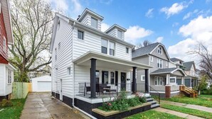 A two-story house with a covered porch, a front yard with a garden, and a visible garage.