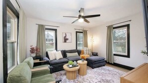 Ein modernes Wohnzimmer mit einer Couch, Sesseln, einem Couchtisch und einem Deckenventilator.