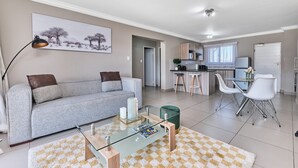 A modern living room with a sofa, coffee table, and a dining area with chairs and a table. - Luxury & Secure apartment - Fourways (Fourways)