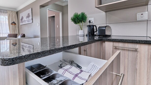 A modern kitchen with a granite countertop, built-in appliances, and a hidden storage space. - Luxury & Secure apartment - Fourways (Fourways)