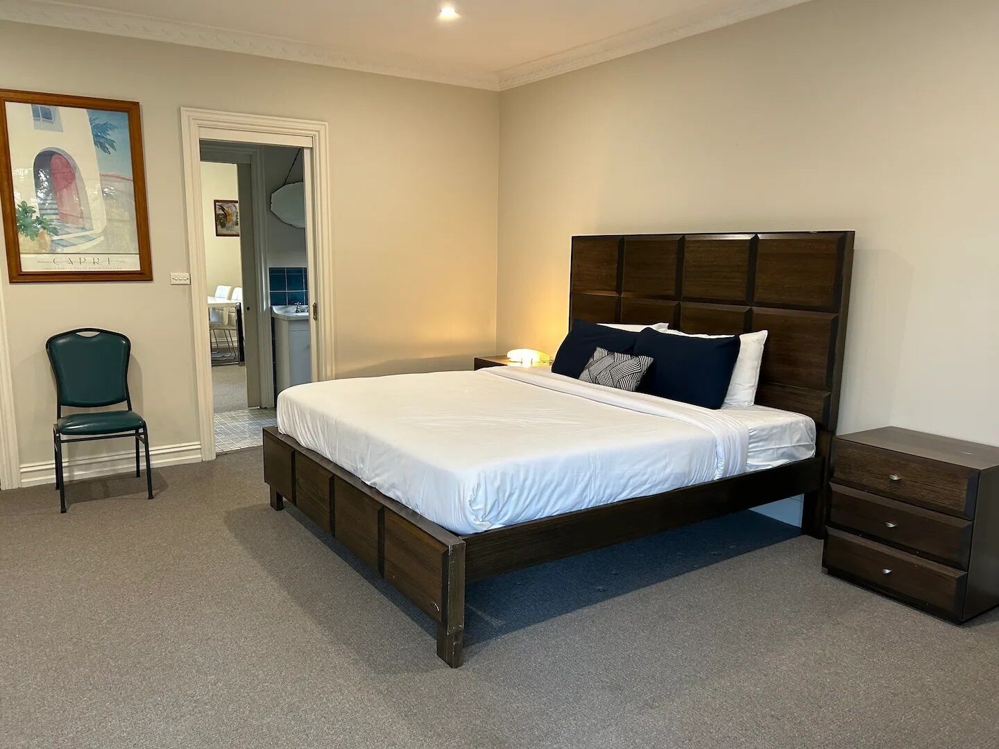 Un dormitorio con una cama grande, una silla, una mesita de noche y un aparador.