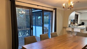 Een eetgedeelte met een grote houten tafel en stoelen, een schuifdeur naar een terras, en een keuken zichtbaar door een boog.