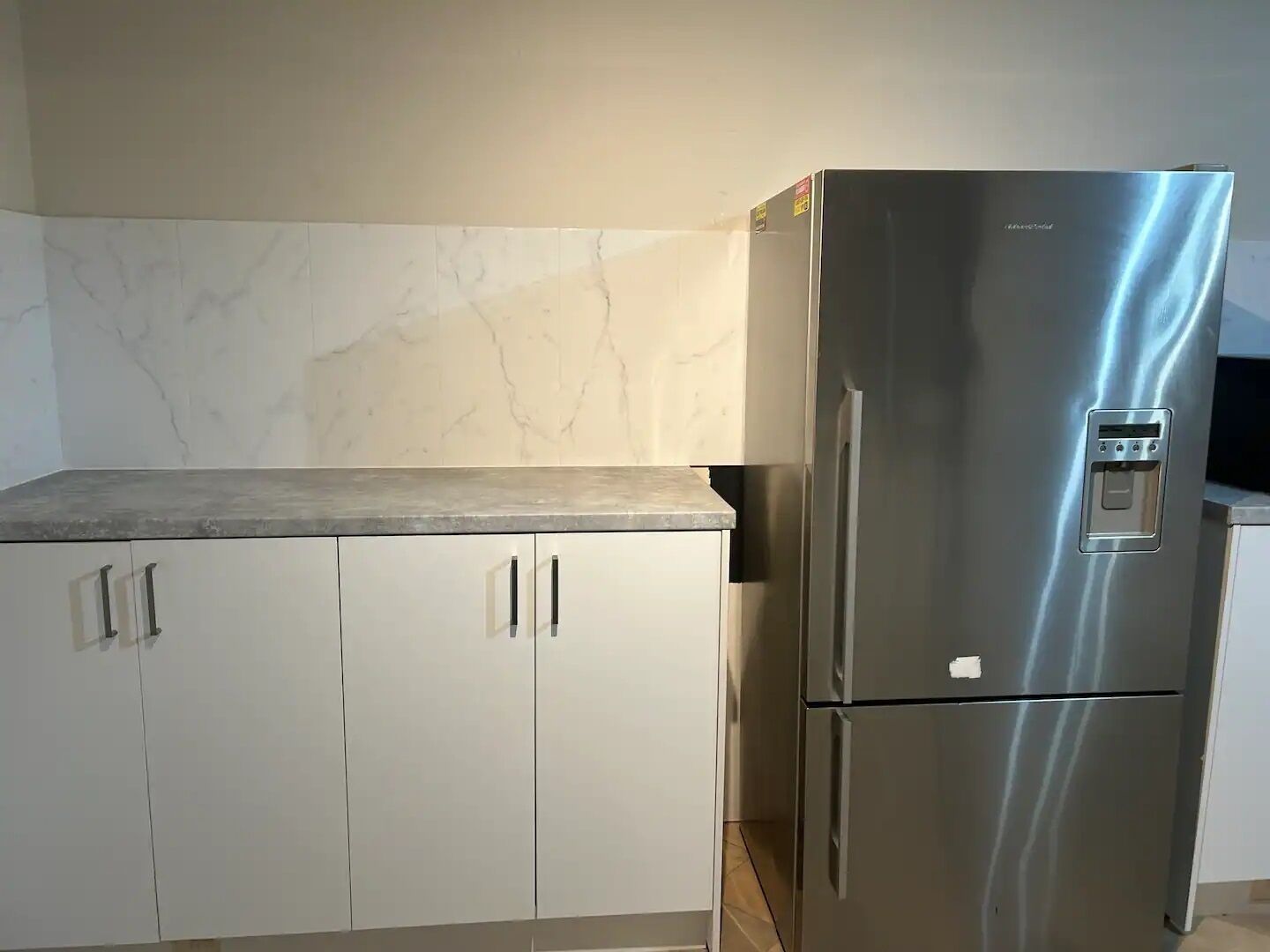 A kitchen with white cabinets, a stainless steel refrigerator, and a marble backsplash.