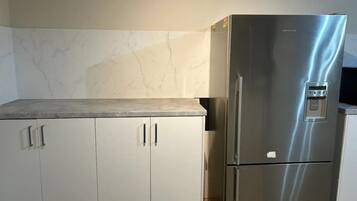 A kitchen with white cabinets, a stainless steel refrigerator, and a marble backsplash.