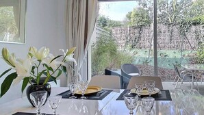 A dining area with a table set for four, large windows, and a view of a garden. - House Six - PLENEUF VAL ANDRE (PLENEUF VAL ANDRE)