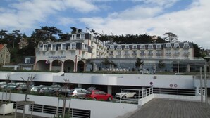 A multi-story hotel with a modern design, featuring balconies and a covered parking area. - House Six - PLENEUF VAL ANDRE (PLENEUF VAL ANDRE)