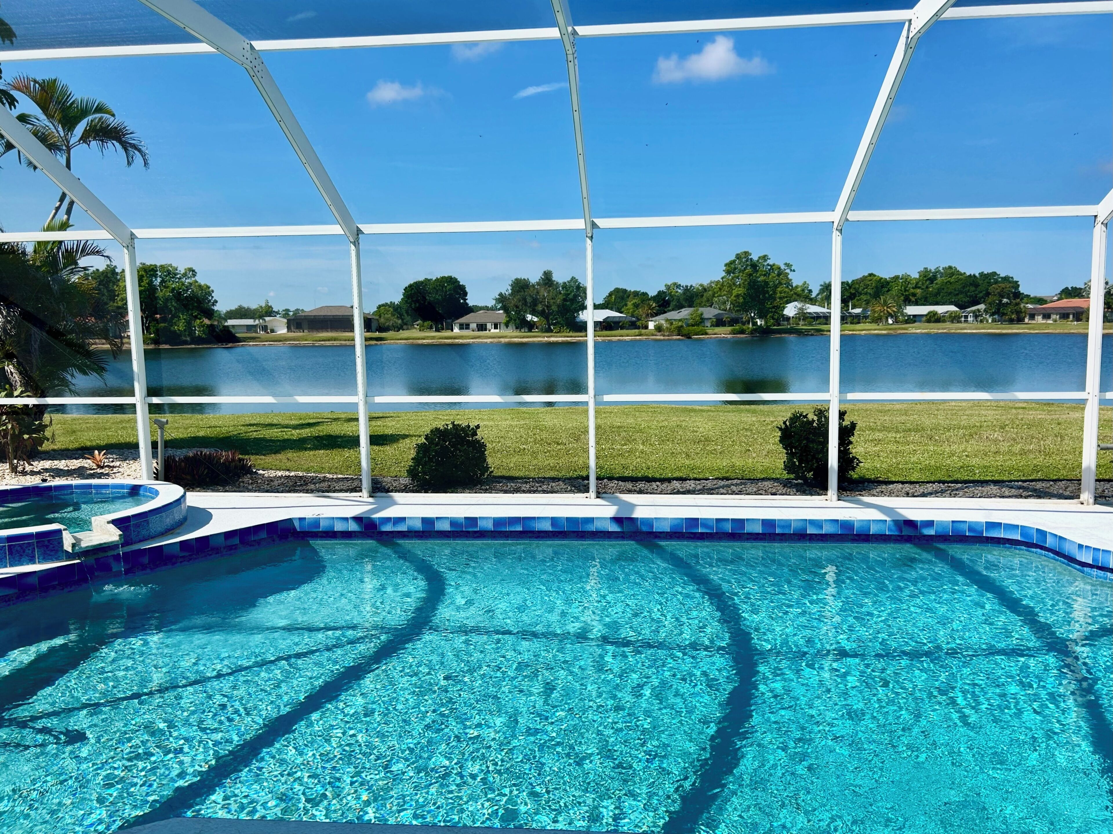 A clear blue swimming pool with a view of a lake and houses in the background.
