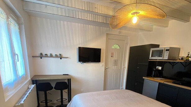 Een compacte hotelkamer met een bed, een klein bureau met twee stoelen, een televisie, een magnetron en een kitchenette.