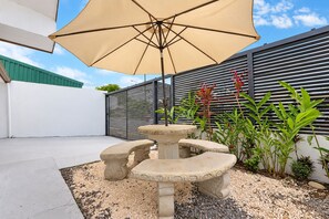 An outdoor seating area with a stone table and chairs, a large umbrella, and a variety of plants.