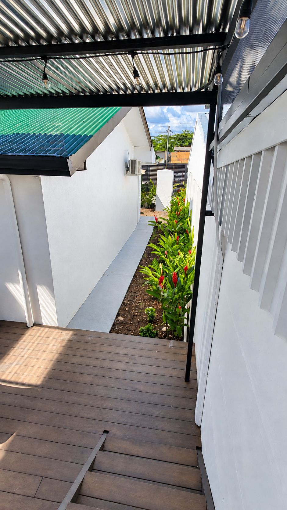 A covered outdoor area with a wooden deck, a garden with red flowers, and a view of a residential street.