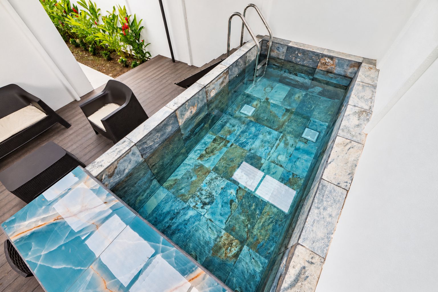 Una piscina rectangular con superficie de agua cristalina, rodeada por una solana con baldosas azules y blancas.