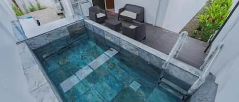 Piscina com cobertura de vidro, pequena área de estar ao ar livre com mesa e cadeiras, e escadaria que leva a um nível superior.