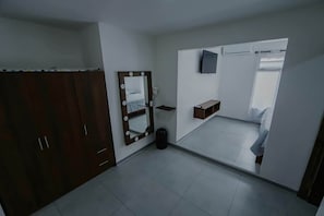 Ein Hotelzimmer mit Kleiderschrank, einem beleuchteten Spiegel, einem kleinen Tisch und einem Bett.