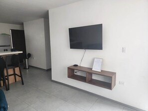 A modern living room with a flat-screen TV mounted on the wall, a wooden TV stand with a remote, and a dining area with a table and chairs. - Casa Monarch La Fortuna • Pool • Volcano Views (La Fortuna)