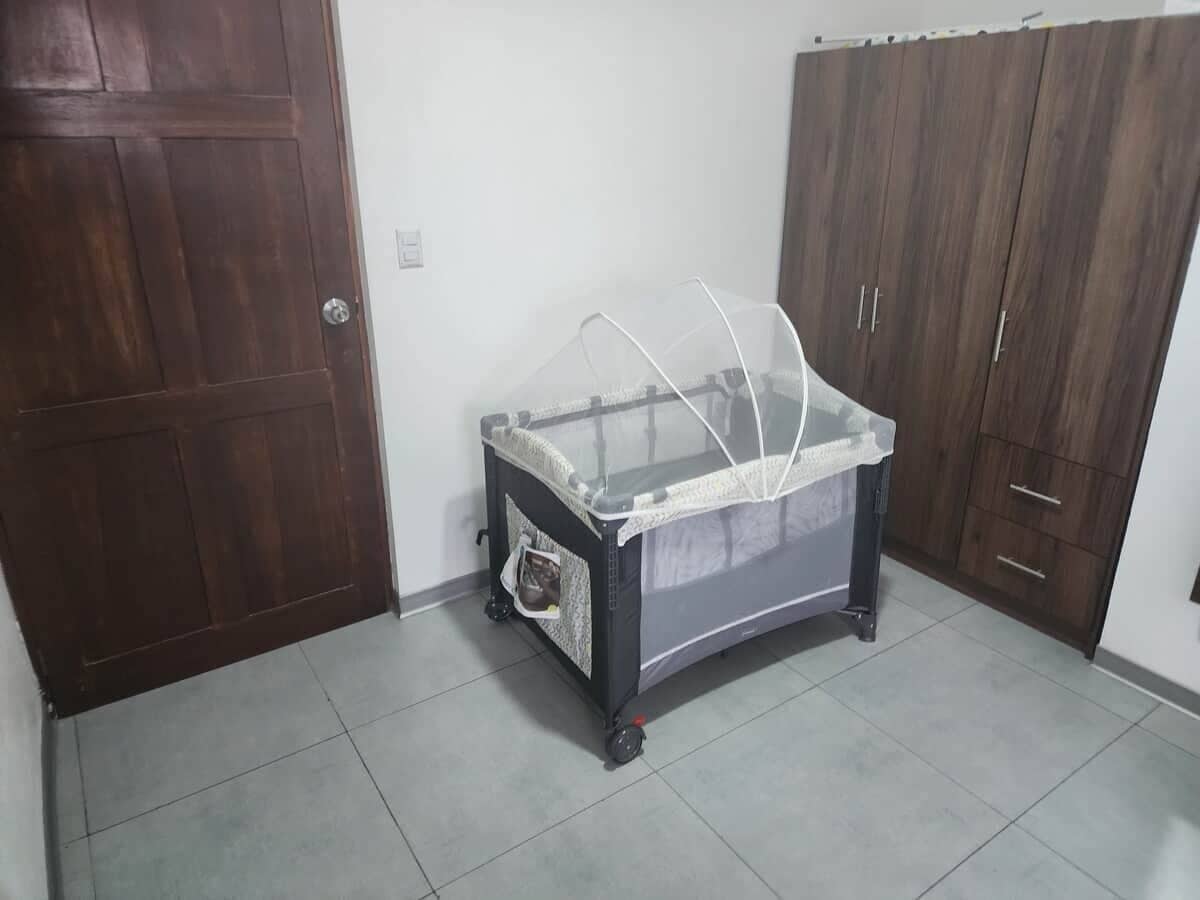 A room with a baby crib, a wooden wardrobe, and a tiled floor.
