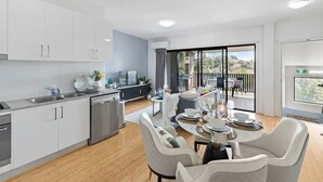 Une cuisine moderne avec des meubles blancs, des appareils en acier inoxydable et un coin repas avec une table dressée pour quatre personnes.