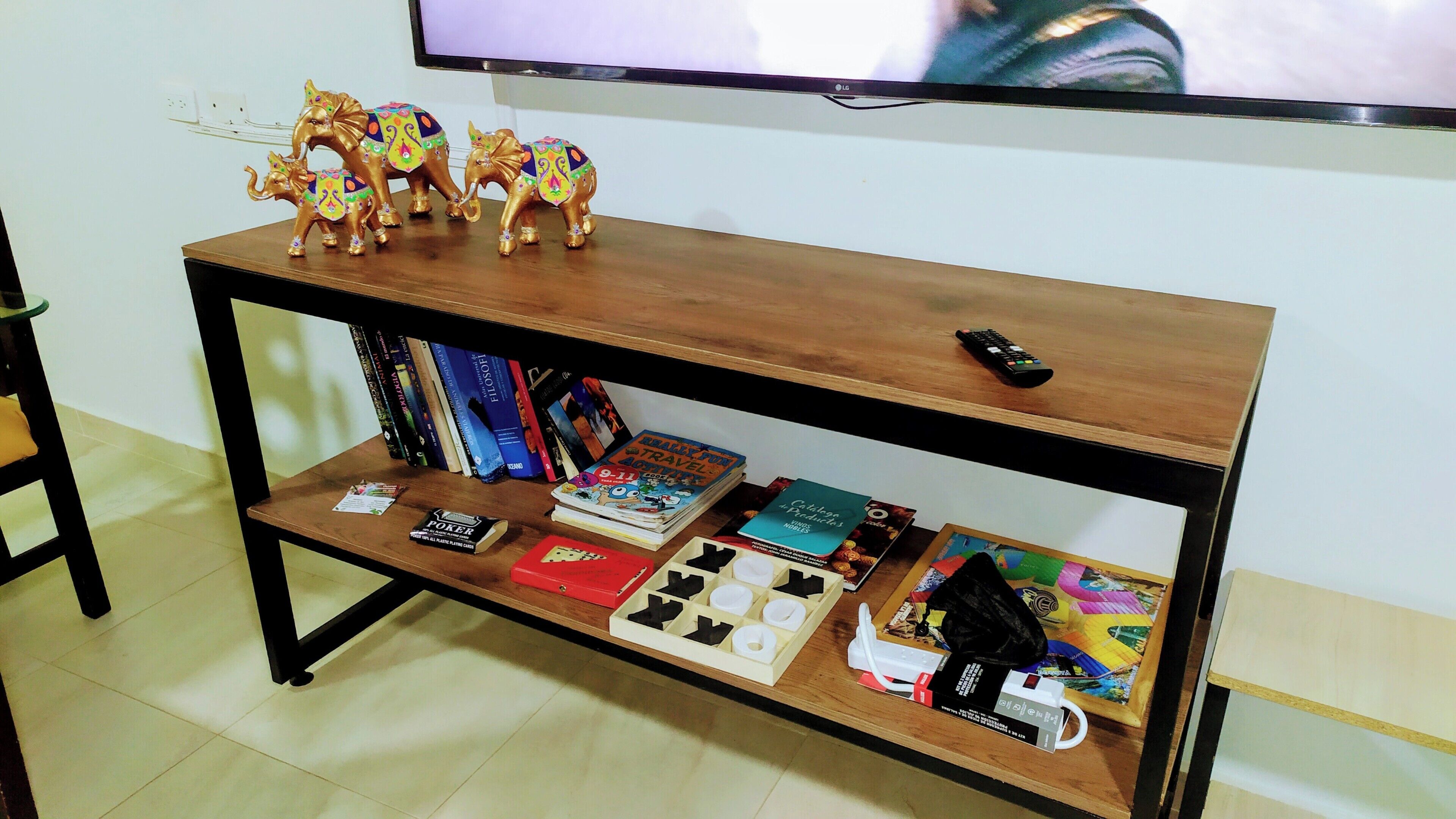 Ein Holz-Fernsehschrank mit einem Flachbildfernseher, Büchern, einer Fernbedienung und dekorativen Elefantfiguren.