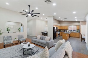 Ein modernes Wohnzimmer mit einem grauen Sofa, gemusterten Sesseln, einem Couchtisch und einem Deckenventilator.