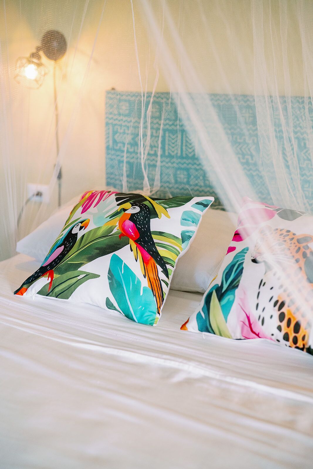 Un letto a baldacchino con cuscini colorati raffiguranti uccelli tropicali e foglie.