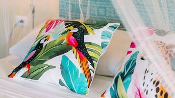 Un letto a baldacchino con cuscini colorati raffiguranti uccelli tropicali e foglie.