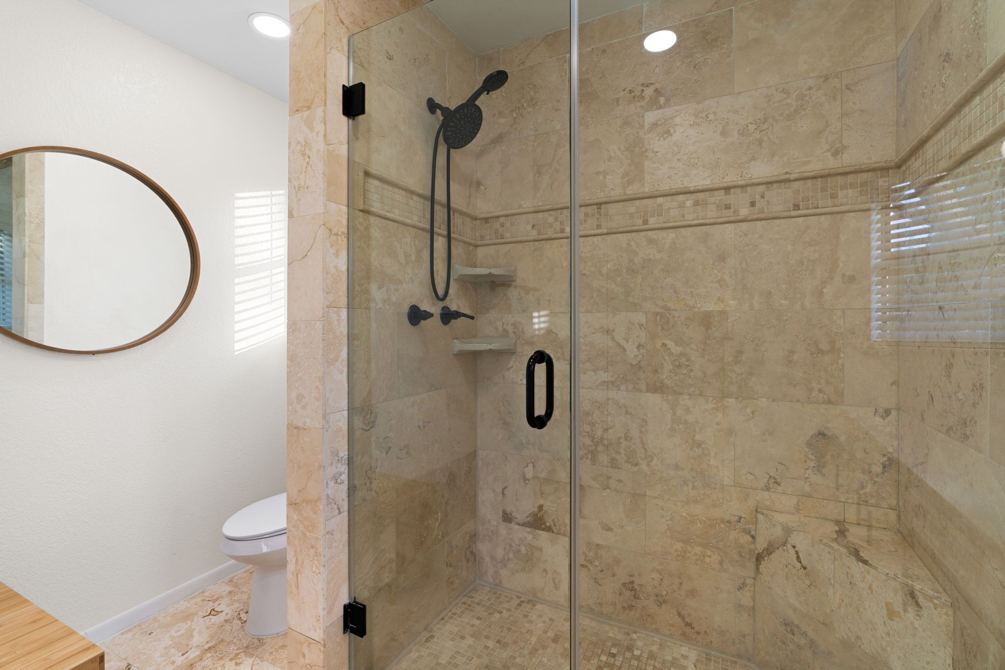 A modern bathroom with a glass-enclosed shower, a toilet, and a mirror.