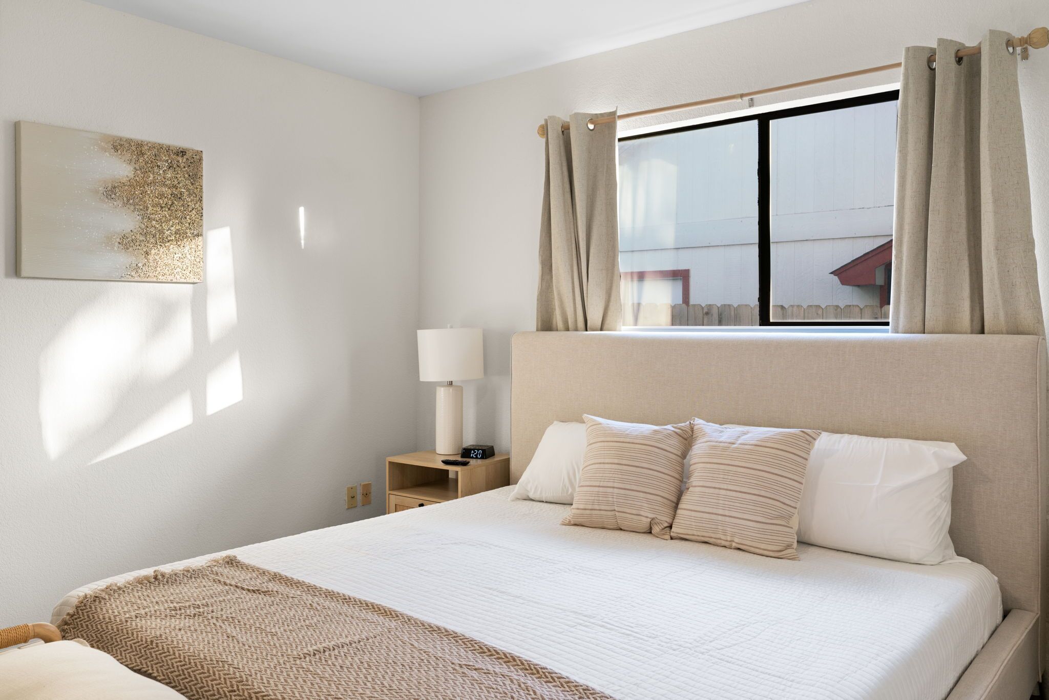 Ein ordentlich eingerichtetes Hotelzimmer mit einem großen Bett, einem Nachttisch mit Lampe und einem Fenster mit Vorhängen.
