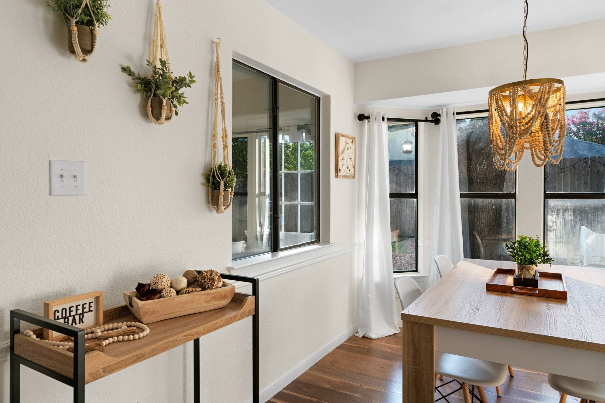 A dining area with a wooden table, chairs, a hanging macrame light fixture, and a window with a view of the outside.
