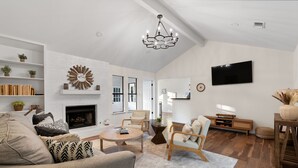 A spacious living room with a fireplace, a chandelier, a television, and a bookshelf. - Charming & Bright W Lounging Pool (Round Rock)