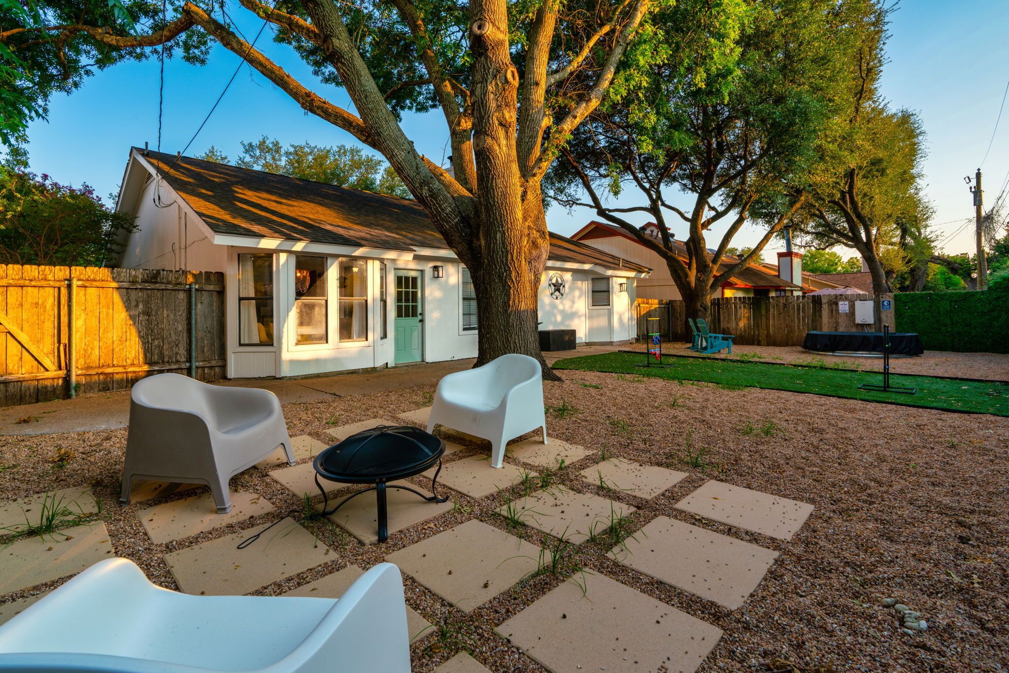 A backyard with a patio area featuring two white plastic chairs and a round table.
