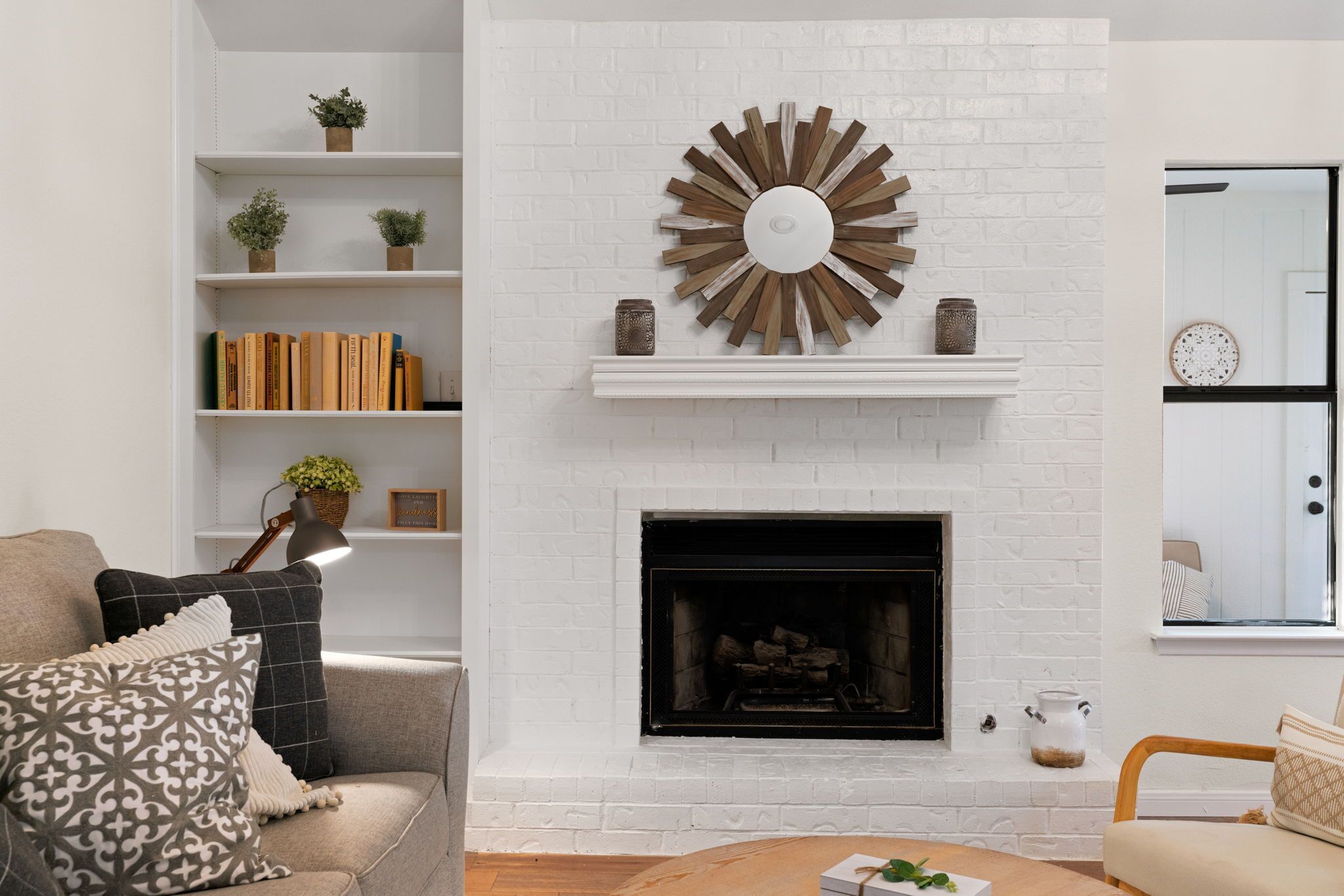 A living room with a white brick fireplace, a bookshelf, and a sofa.